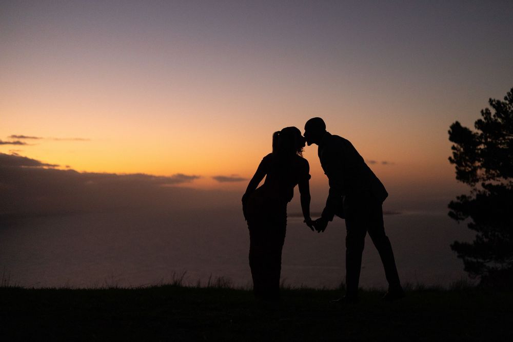 Silhouetted figures stand on a hilltop against a dramatic sunset sky creating a peaceful outdoor scene.