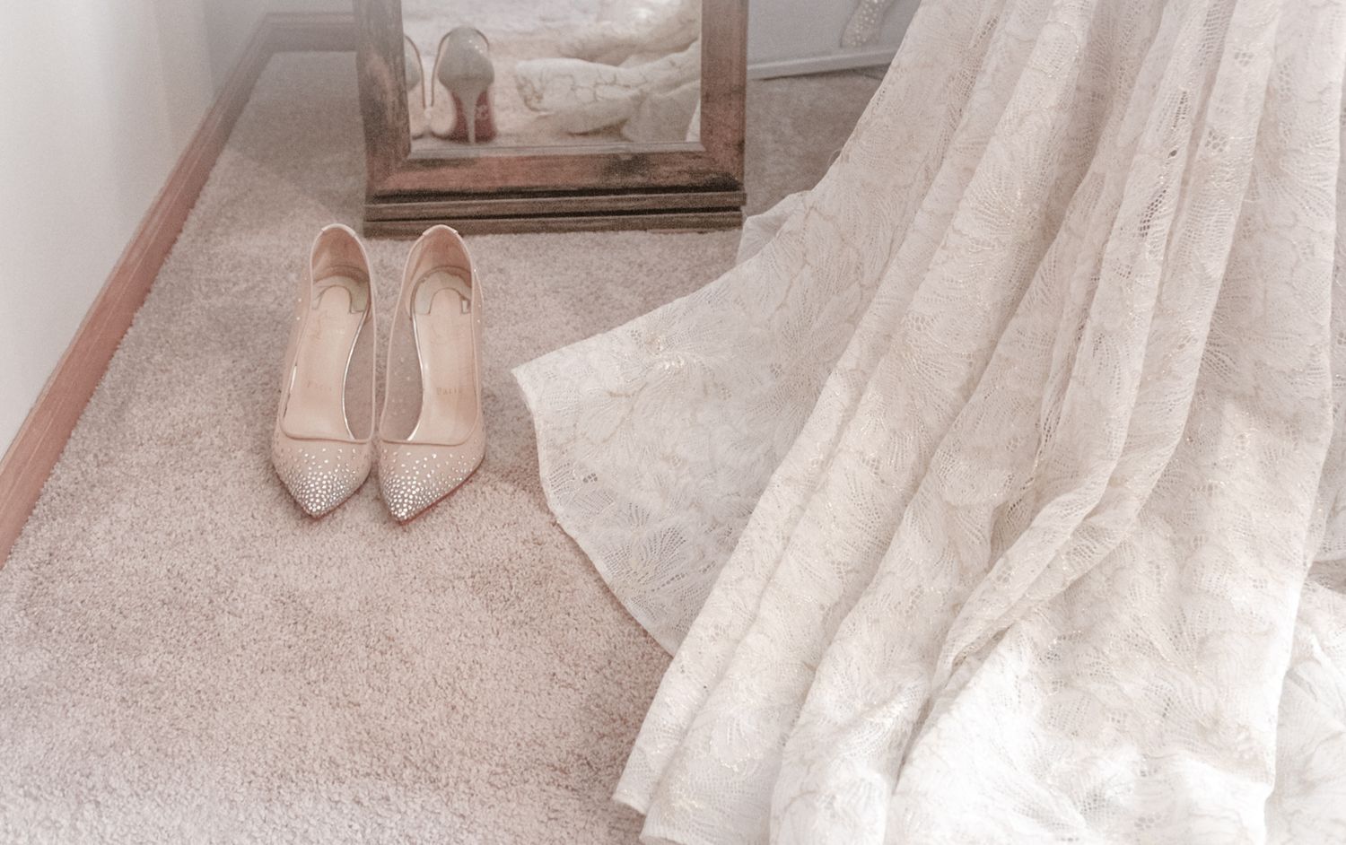 Close-up detail of satin ballet flats and flowing wedding dress hem on soft beige carpet.