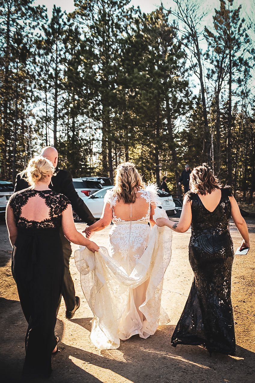 A group in matching black and cream dresses dances in a line against a backdrop of tall pine trees at sunset.