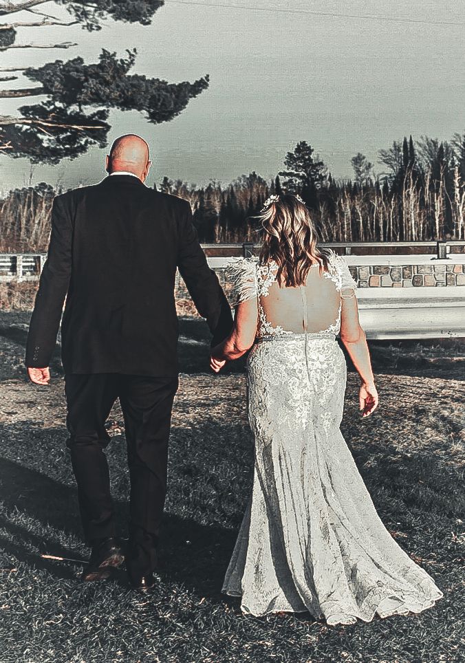 A couple wearing black suit and white lace dress walking through a rustic outdoor setting in a romantic photoshoot.