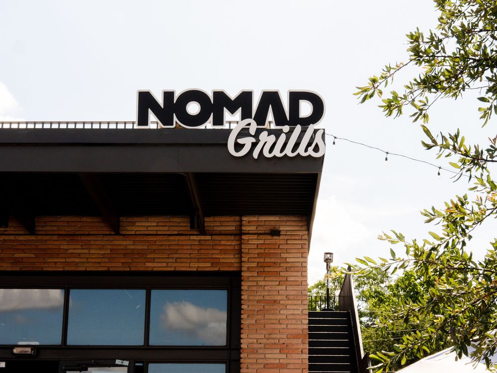 Modern storefront signs for Nomad and Onlus businesses mounted on brick buildings with leafy trees overhead.