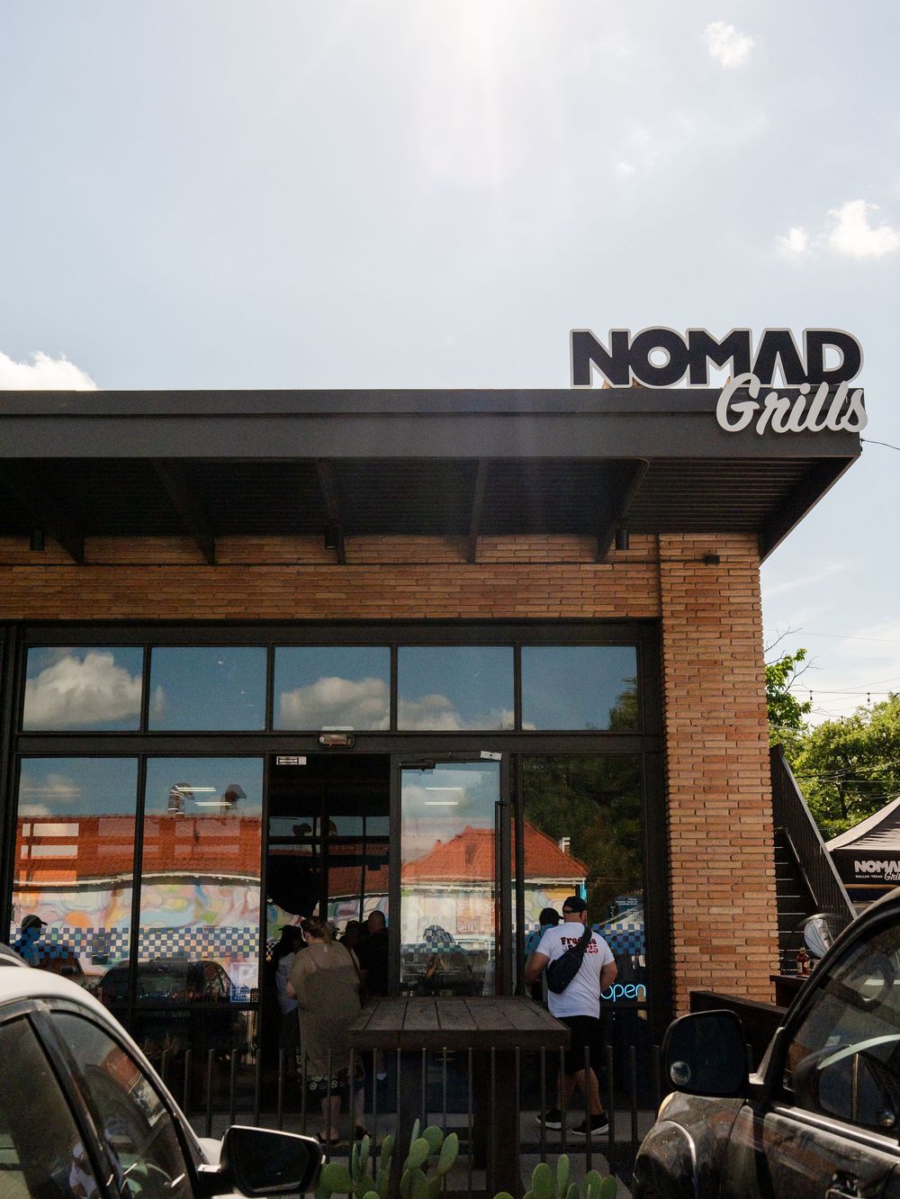 Exterior view of Nomad Grills and O'Reilly Auto Parts storefront in a brick commercial building on a sunny day.