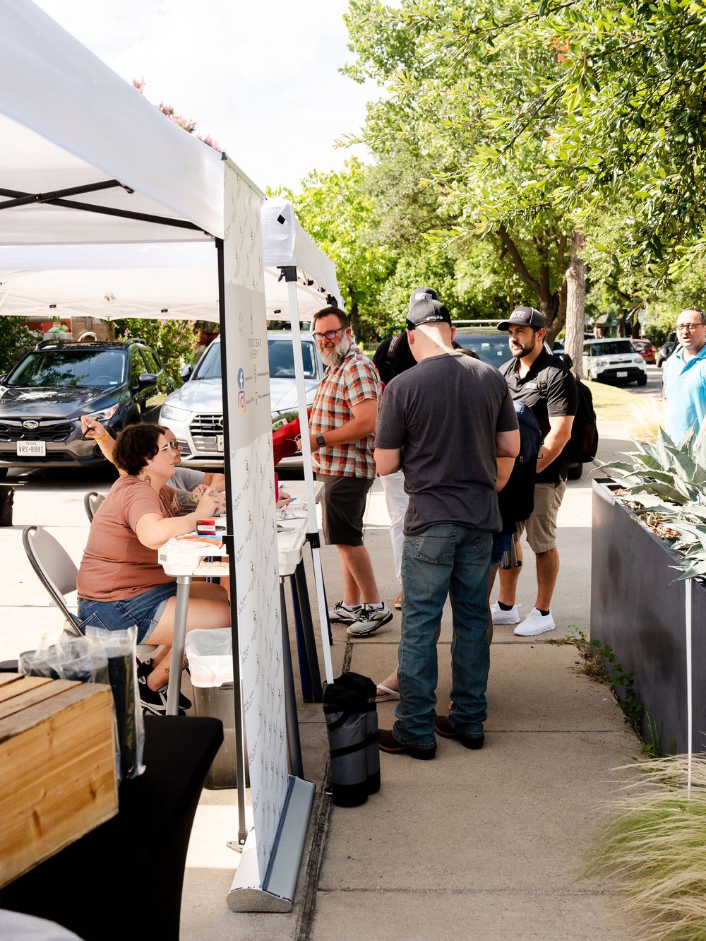 People stand in line at a covered outdoor food service counter during a catered event.