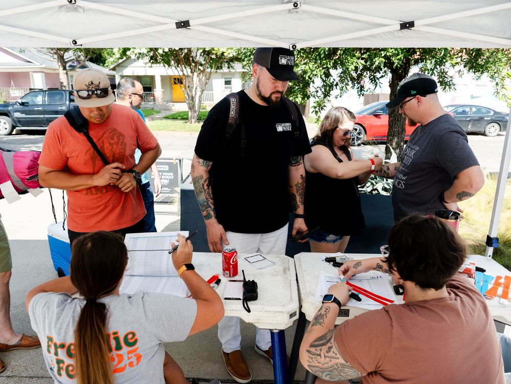 People gather around a table at an outdoor event signing papers and documents.