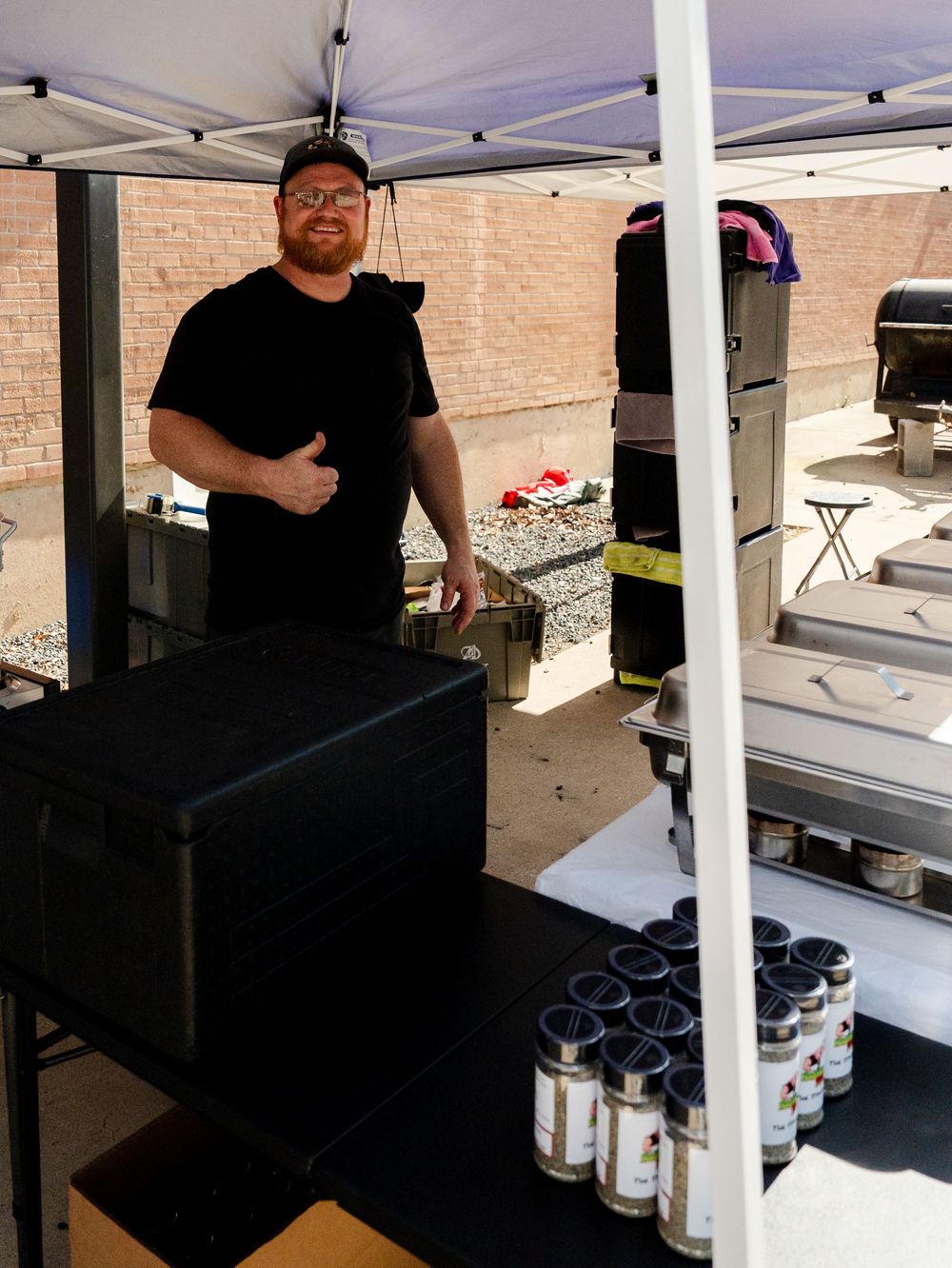 Workers set up a white canopy tent with tables and equipment underneath during an outdoor event preparation.