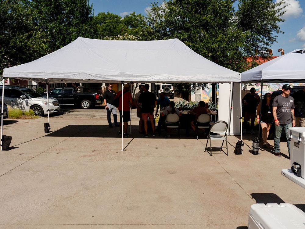 White canopy tents set up in a row on a concrete surface at an outdoor event venue on a sunny day.