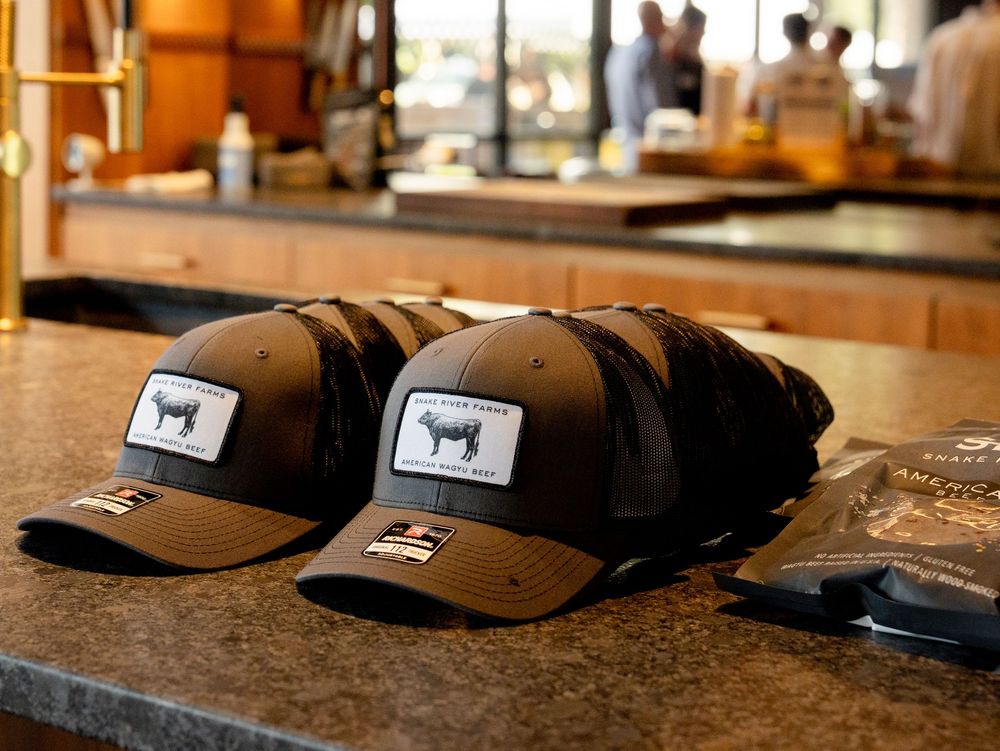 Baseball caps with cow logo designs displayed on wooden retail counter at Yeti brand merchandise store.