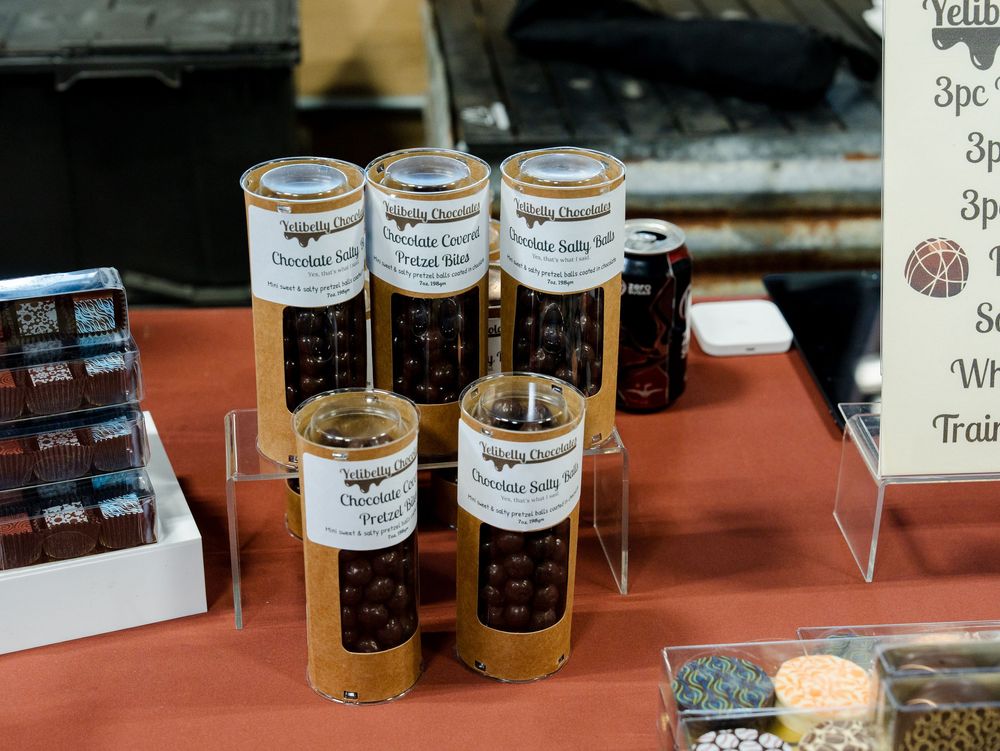 Various jars of preserves and condiments displayed on a rustic retail shelf with price tags and labels.