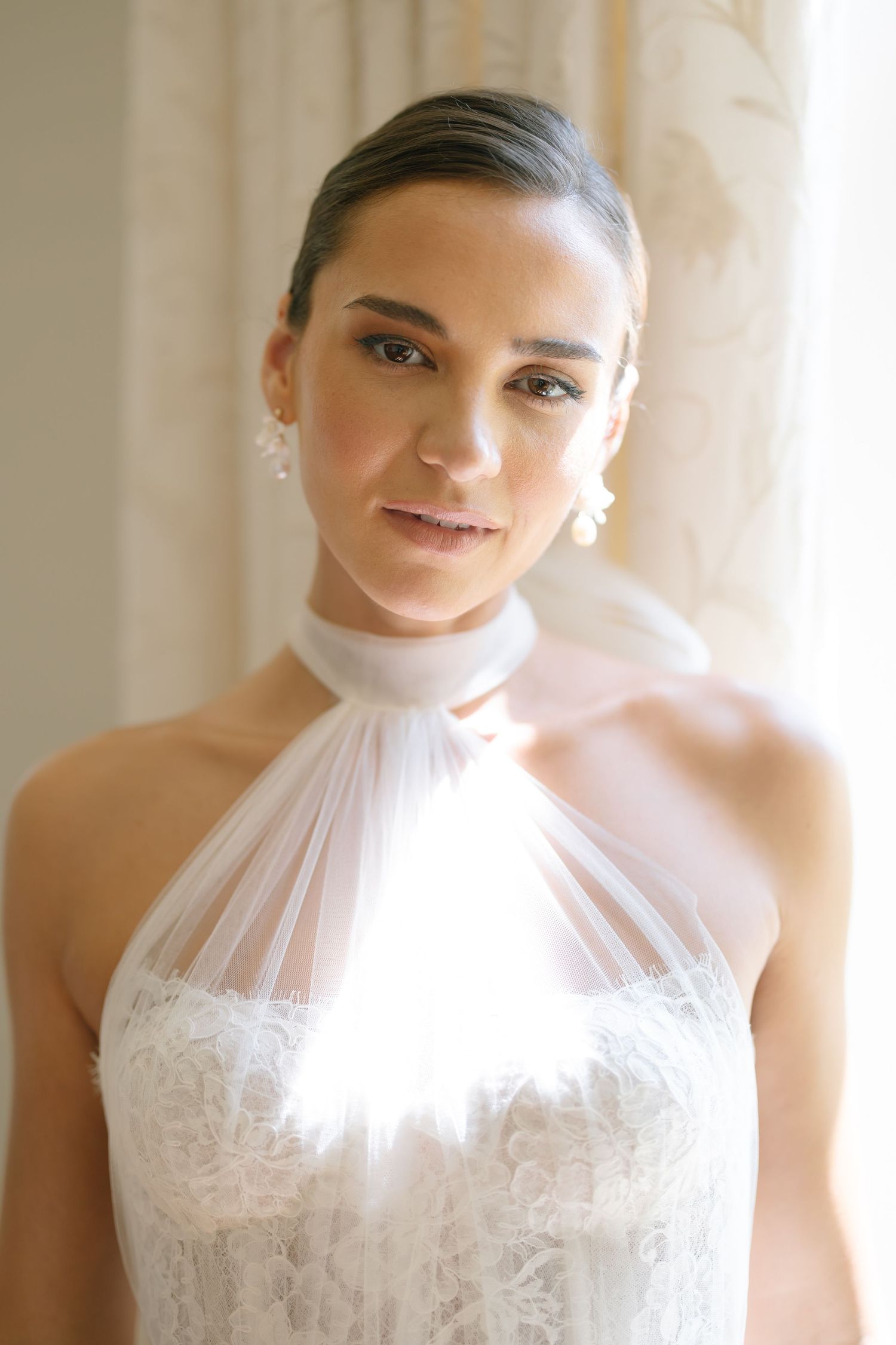 A high-neck wedding gown with delicate tulle and lace details photographed in soft window light.