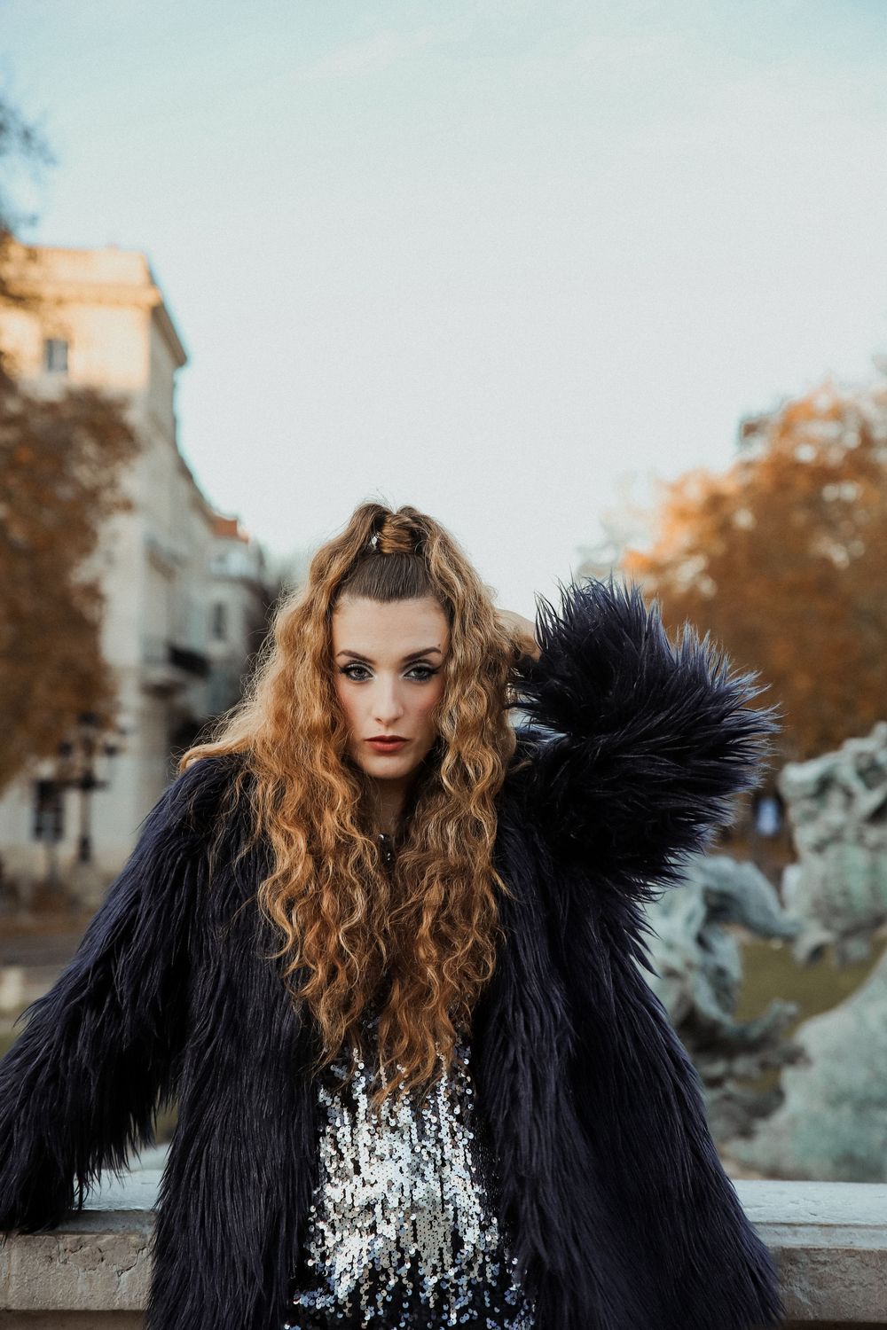A series of fashion portraits showing someone with curly blonde hair wearing a dramatic black fur coat in an outdoor setting.