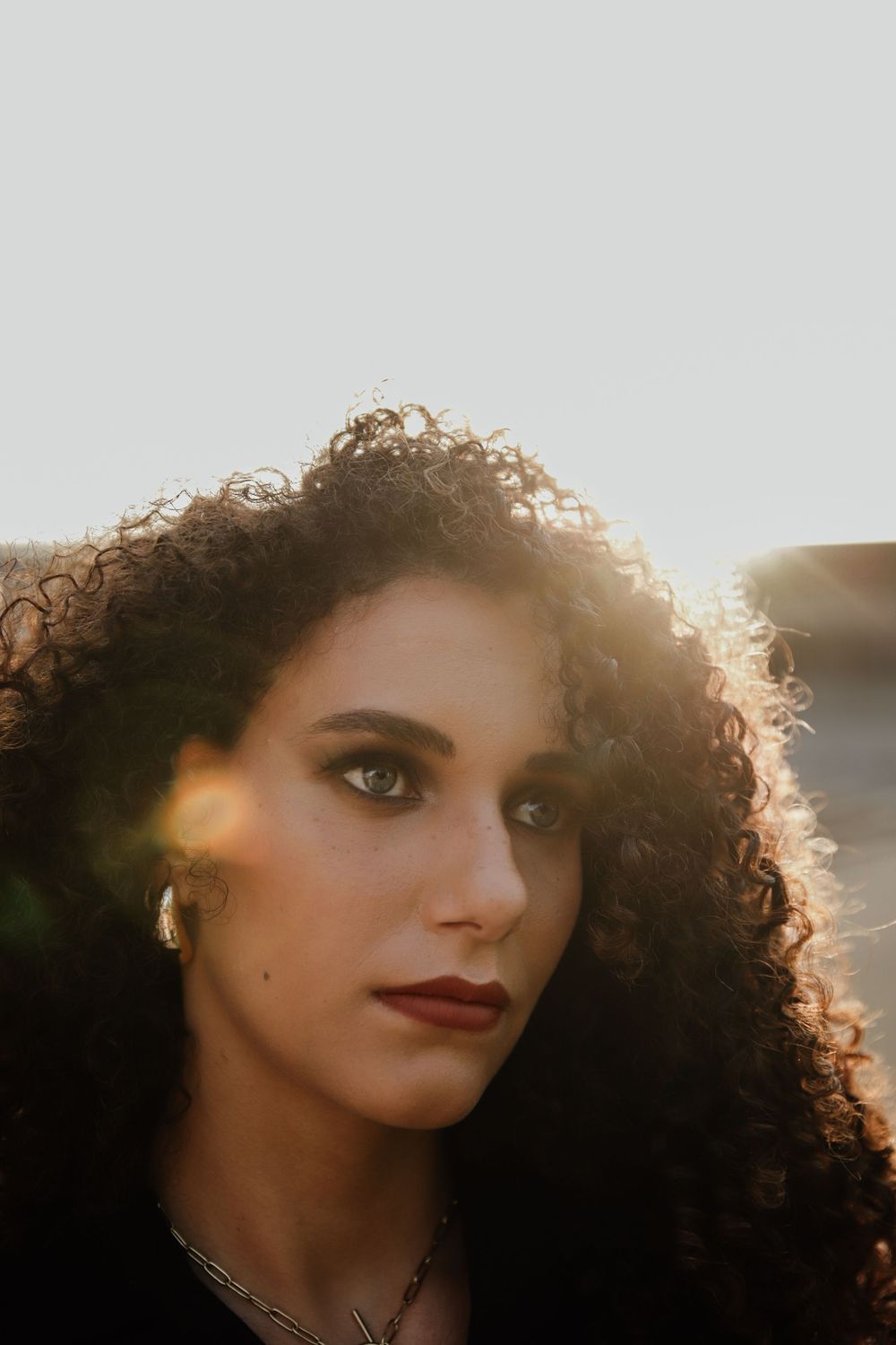 Portrait with backlit curly hair and red lipstick against sunset light creating a golden glow effect.