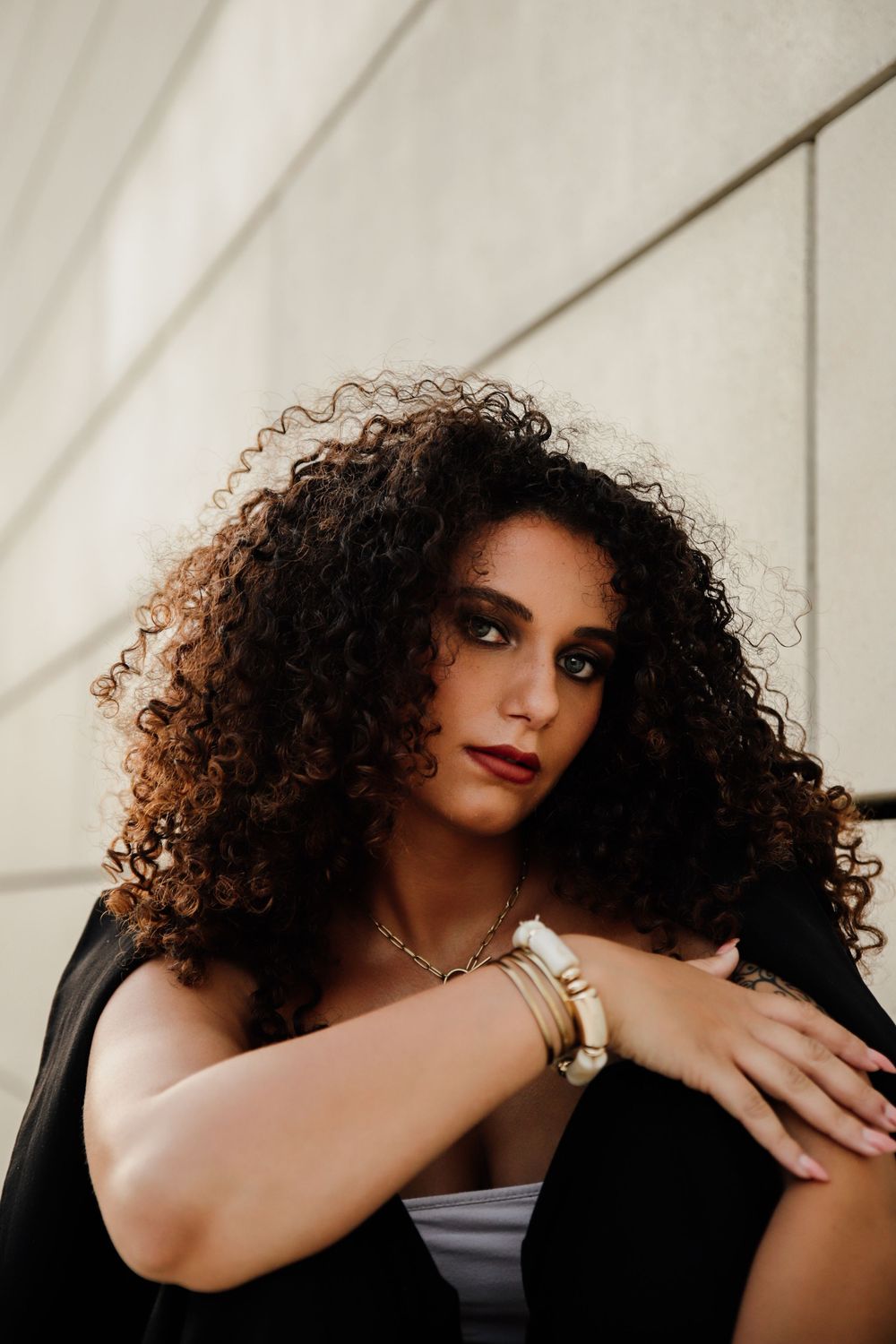 Portrait of person with voluminous natural curly dark hair and red lipstick wearing black against light background.