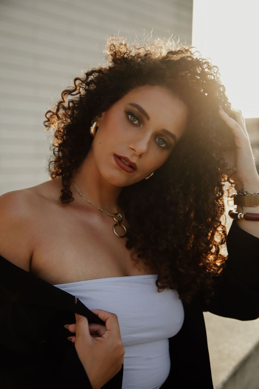 Dramatic backlit sunset portraits showing someone with curly hair in soft golden lighting wearing a white strapless top.