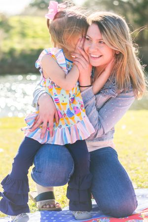 Mother and child share playful moments in a sunny outdoor setting with beautiful bokeh background.