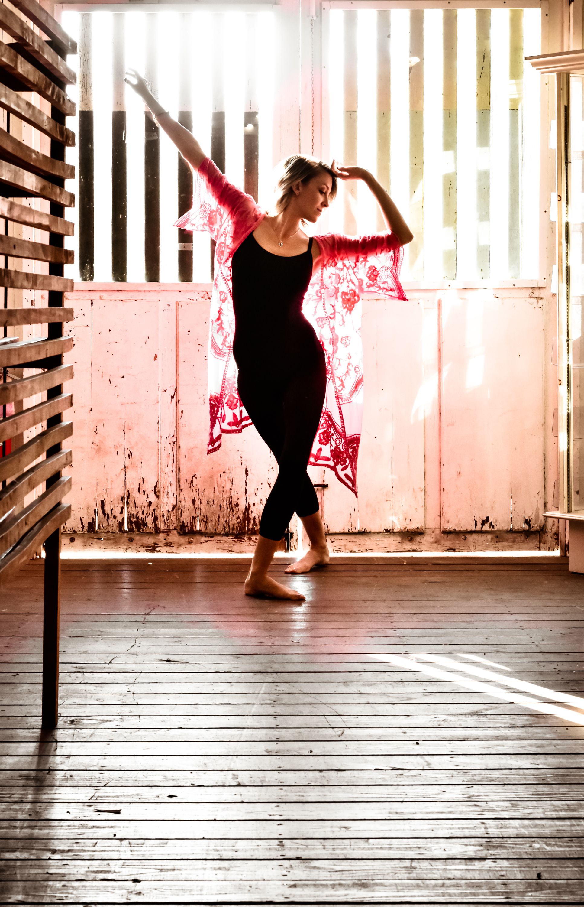 Dancer performs elegant movements in vintage studio with dramatic lighting and wooden floors.