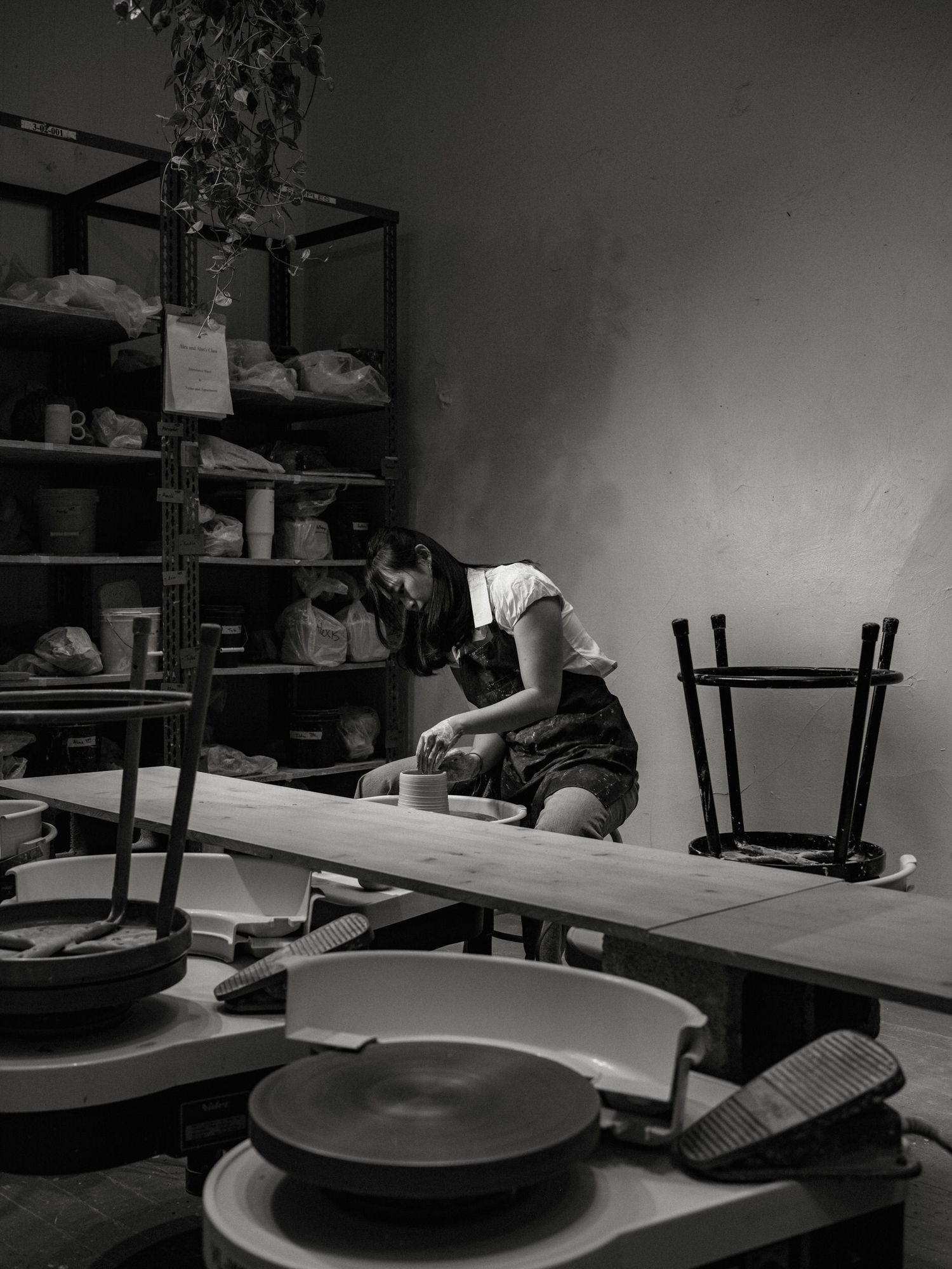 Black and white image of a pottery studio workshop with multiple wheels and work surfaces.