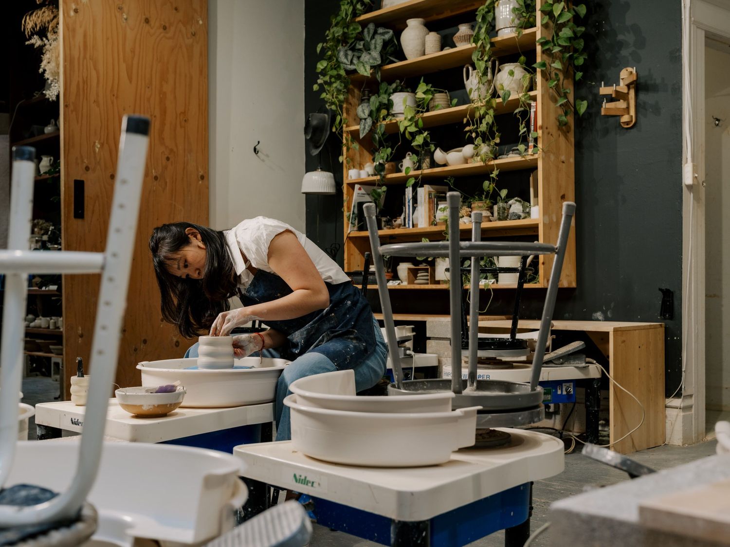 Wide view of a pottery studio showing multiple workstations and organized shelving units.