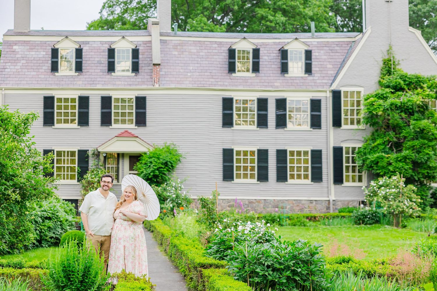 White colonial home with black shutters and a blooming garden path leading to the front entrance in spring.