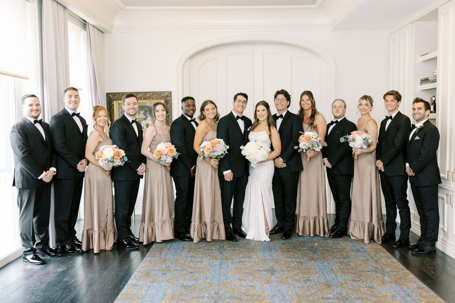 An outdoor autumn wedding ceremony with a white floral arch and fall foliage in the background.