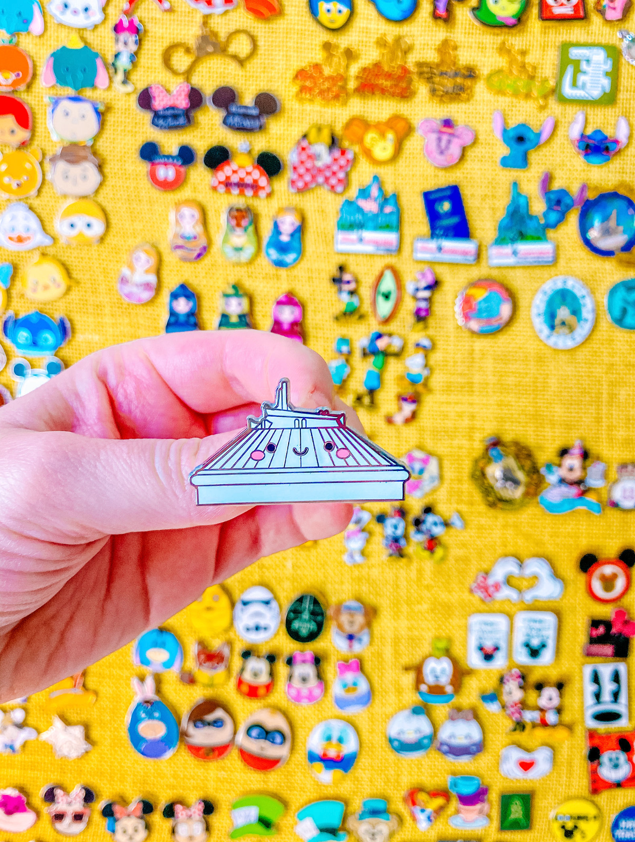 Hand holding Space Mountain attraction pin against background of Disney pin collection.