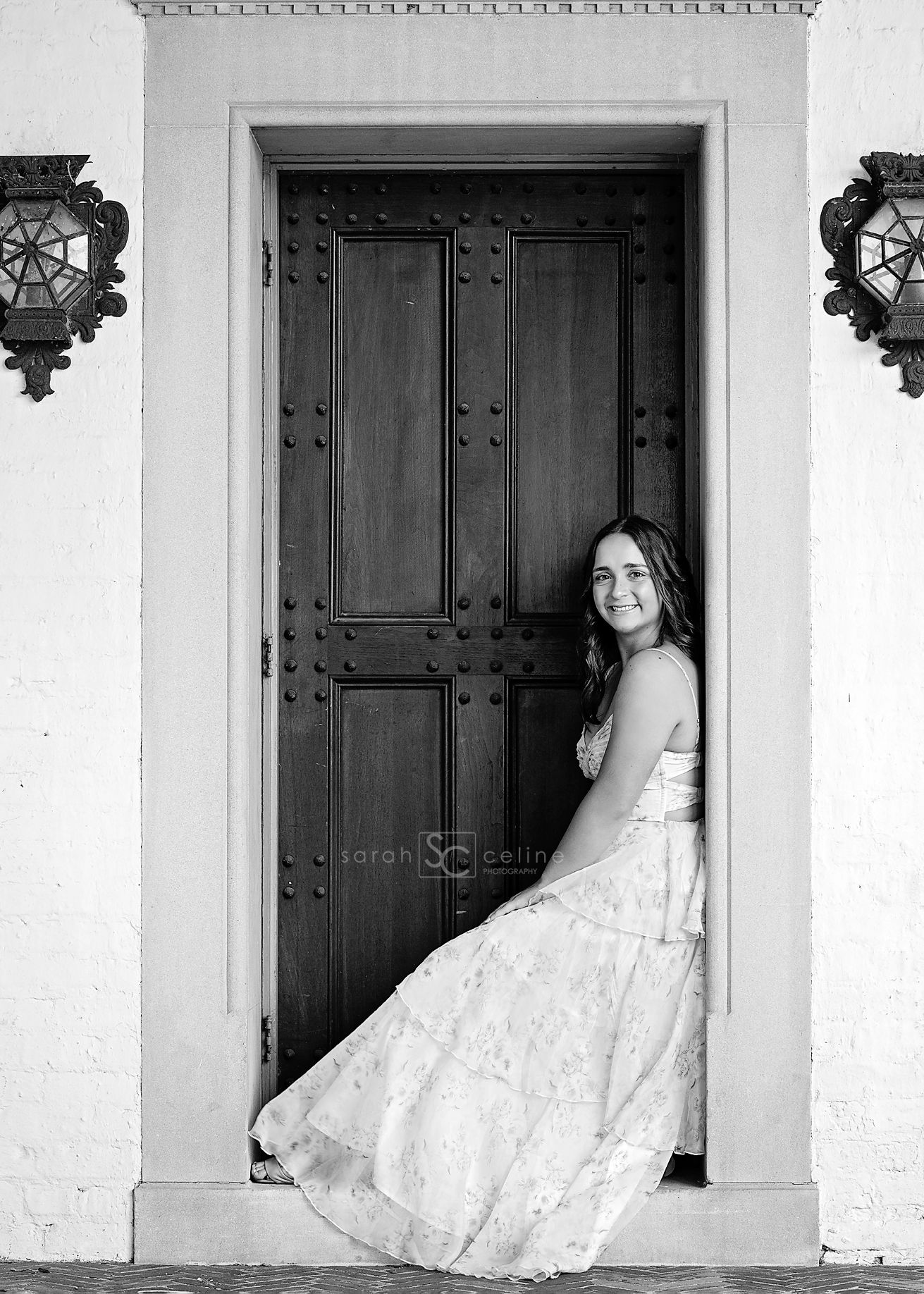 Black and white wedding portrait showing someone in a lacy white dress posing in an ornate doorway with vintage sconces.