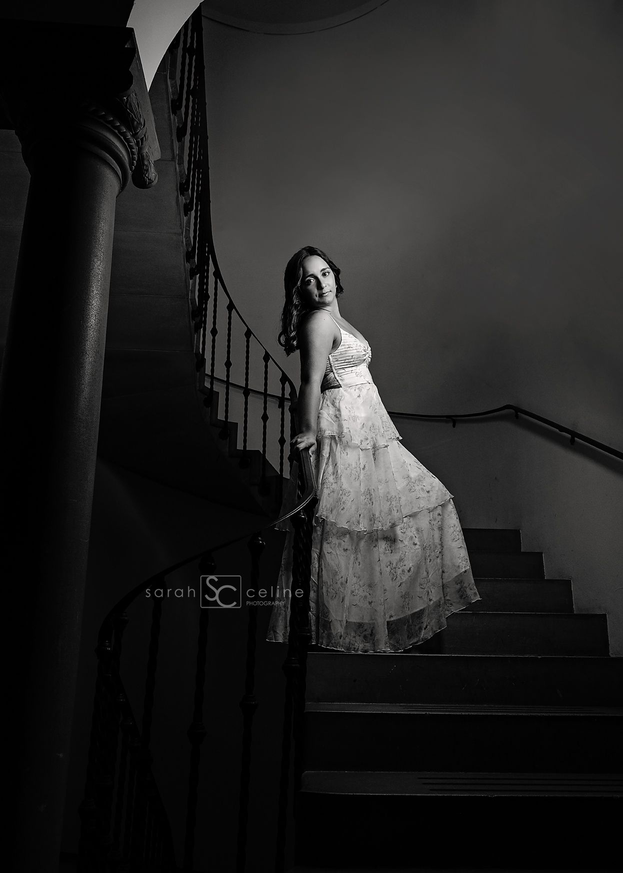 A dramatic black and white photo on a curved staircase shows a person in an elegant lace dress leaning against the railing.