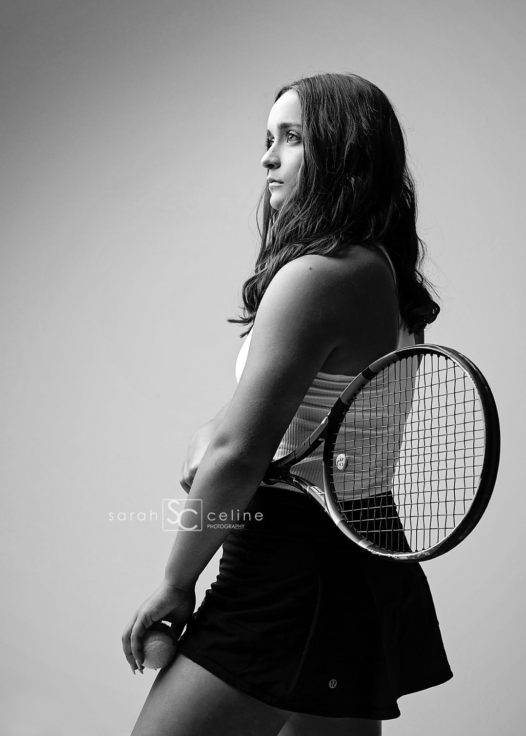 Black and white portrait of a tennis player in profile holding a racquet, wearing athletic attire against a light backdrop.