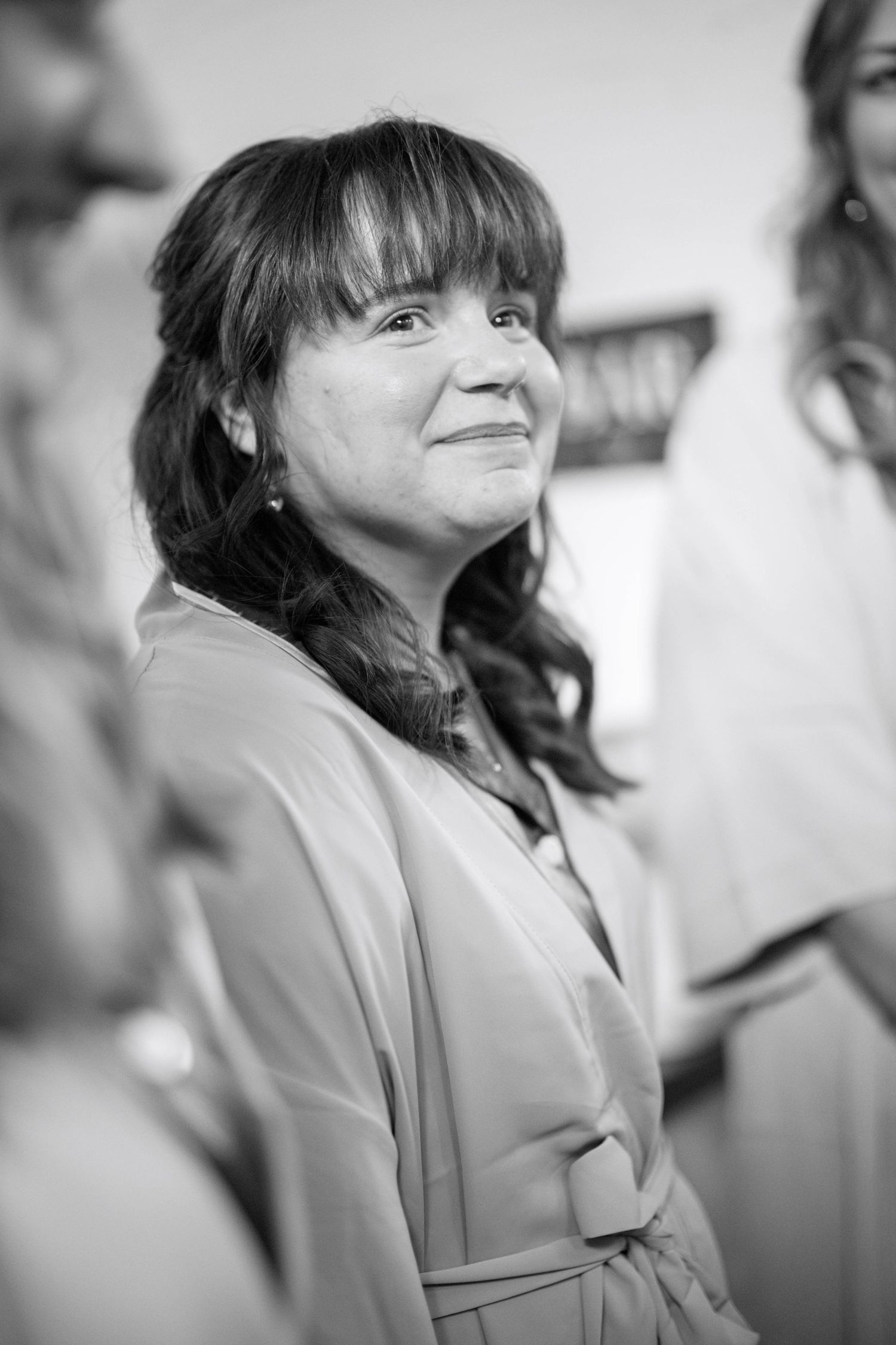 A close-up black and white portrait showing a person in a light-colored coat smiling warmly to the side.