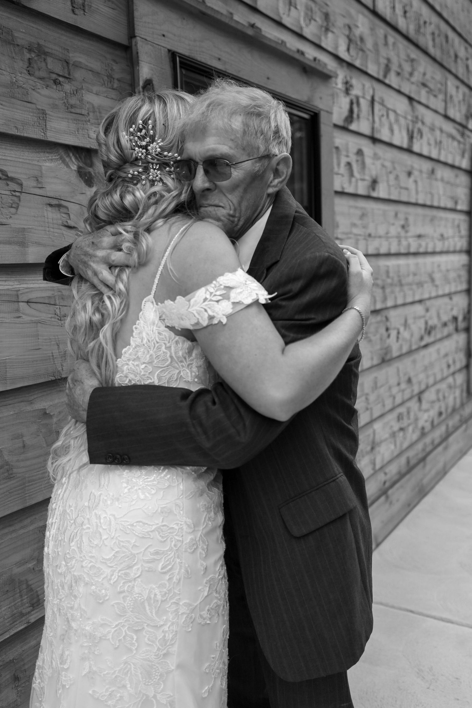 A touching black and white wedding moment shows an emotional embrace between a bride in lace and an elderly man in a suit.