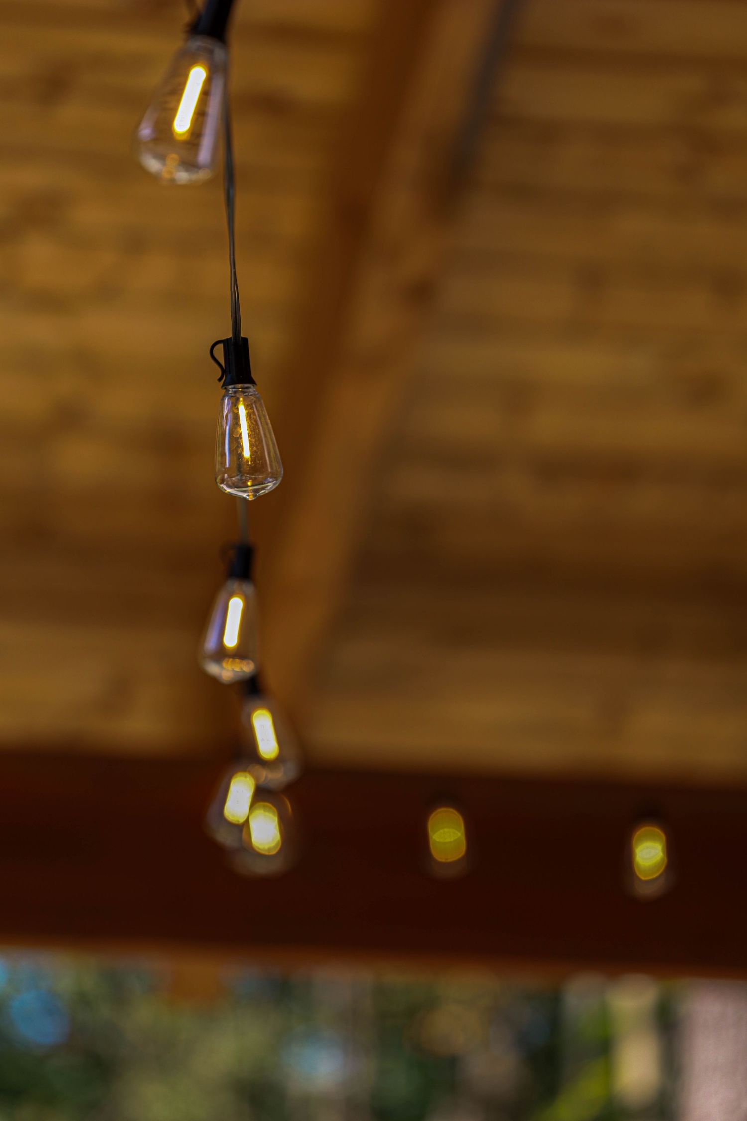 String of Edison bulb lights hanging from wooden ceiling beams create warm ambient lighting.