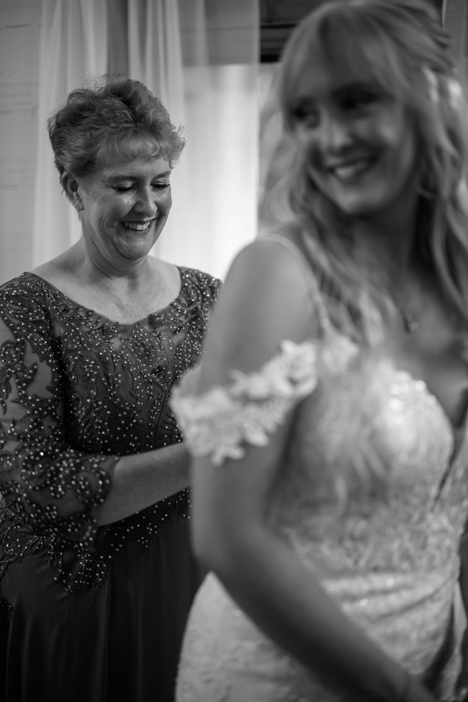 A tender black and white moment showing two women sharing emotions at a wedding, one in a sparkly dress and one in white.