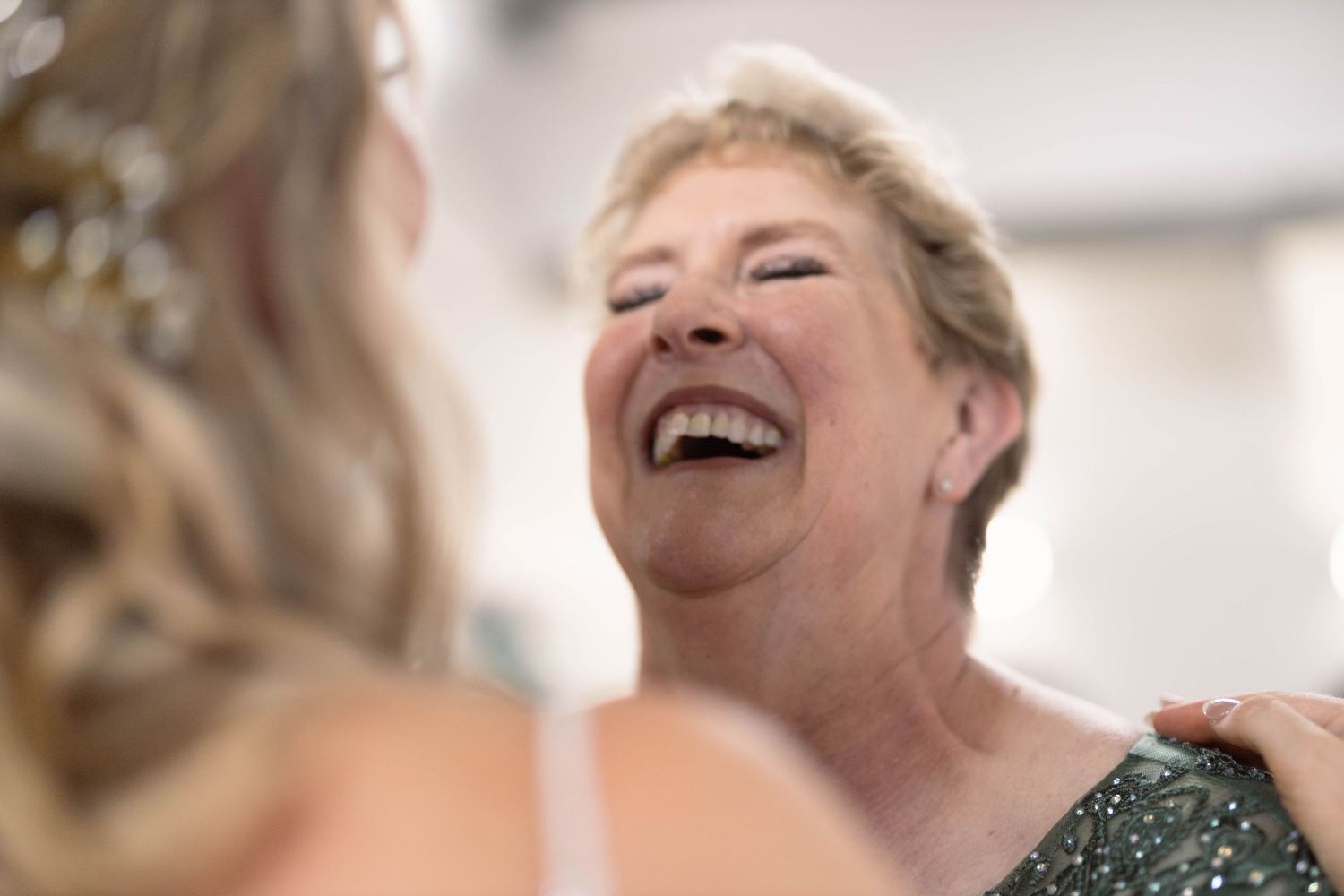 A joyful senior wearing a green sequined dress laughs heartily during what appears to be a special occasion.
