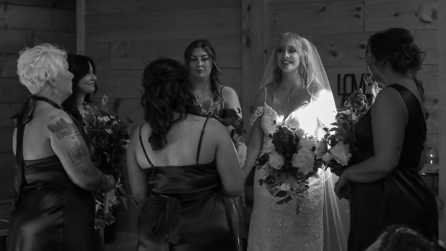 Wedding party gathers for group celebration in elegant indoor venue with floral decorations and formal attire.