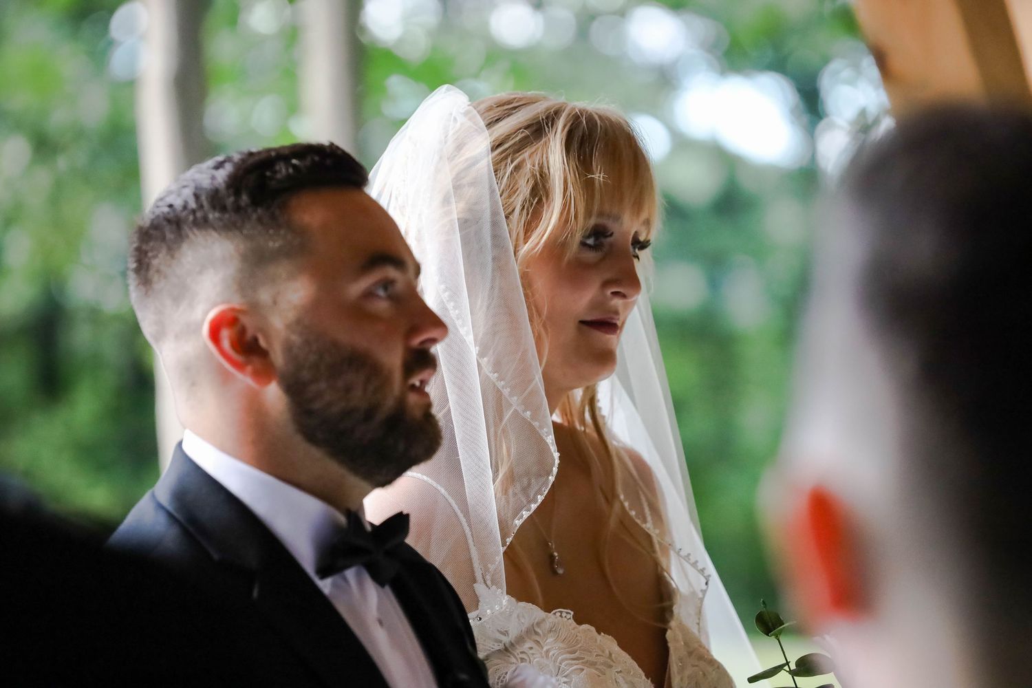 A couple shares an intimate embrace during their wedding ceremony in an outdoor garden setting.