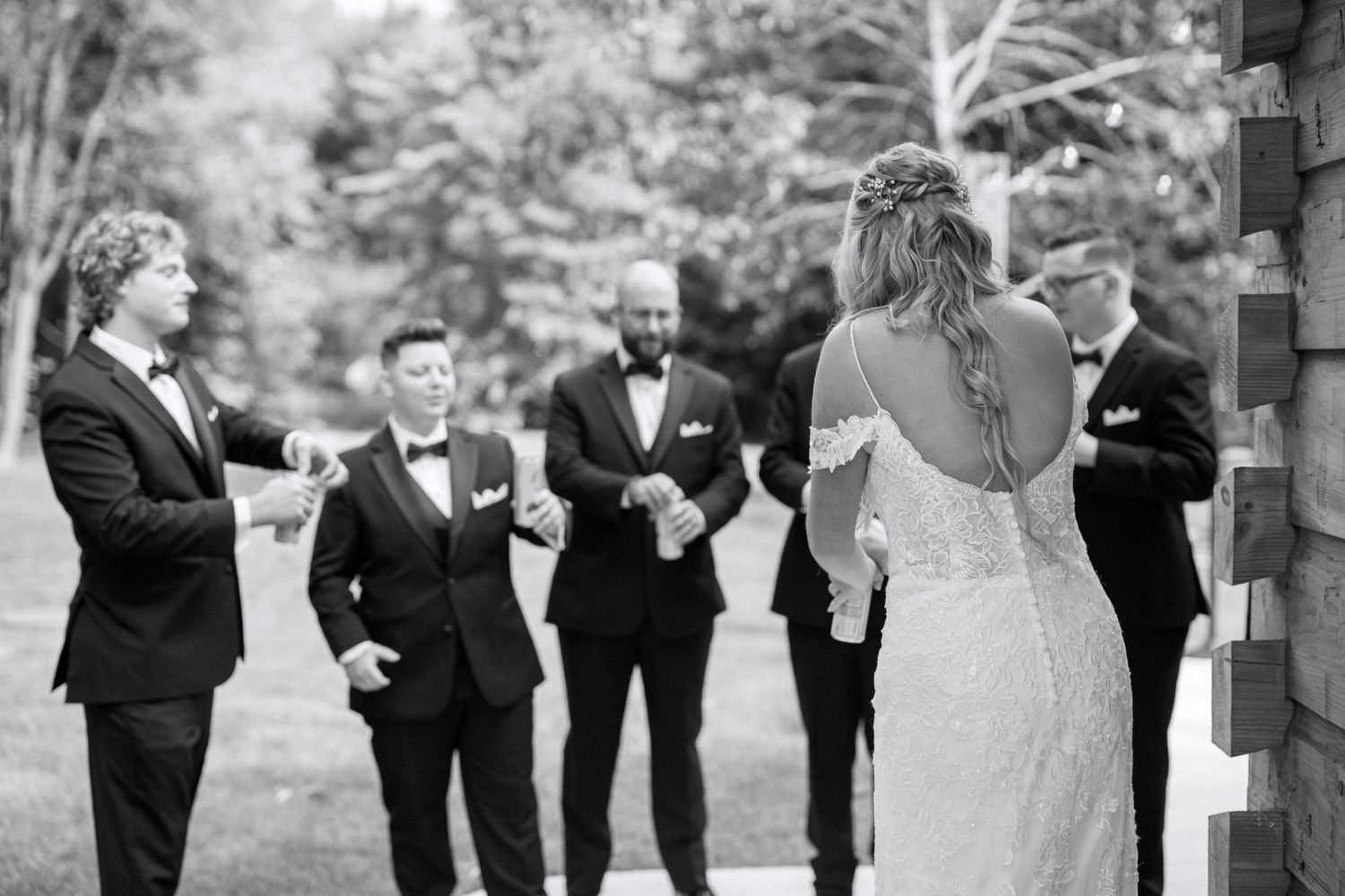 A bridal party in formal attire walks together along a garden path during a black and white wedding photo session.