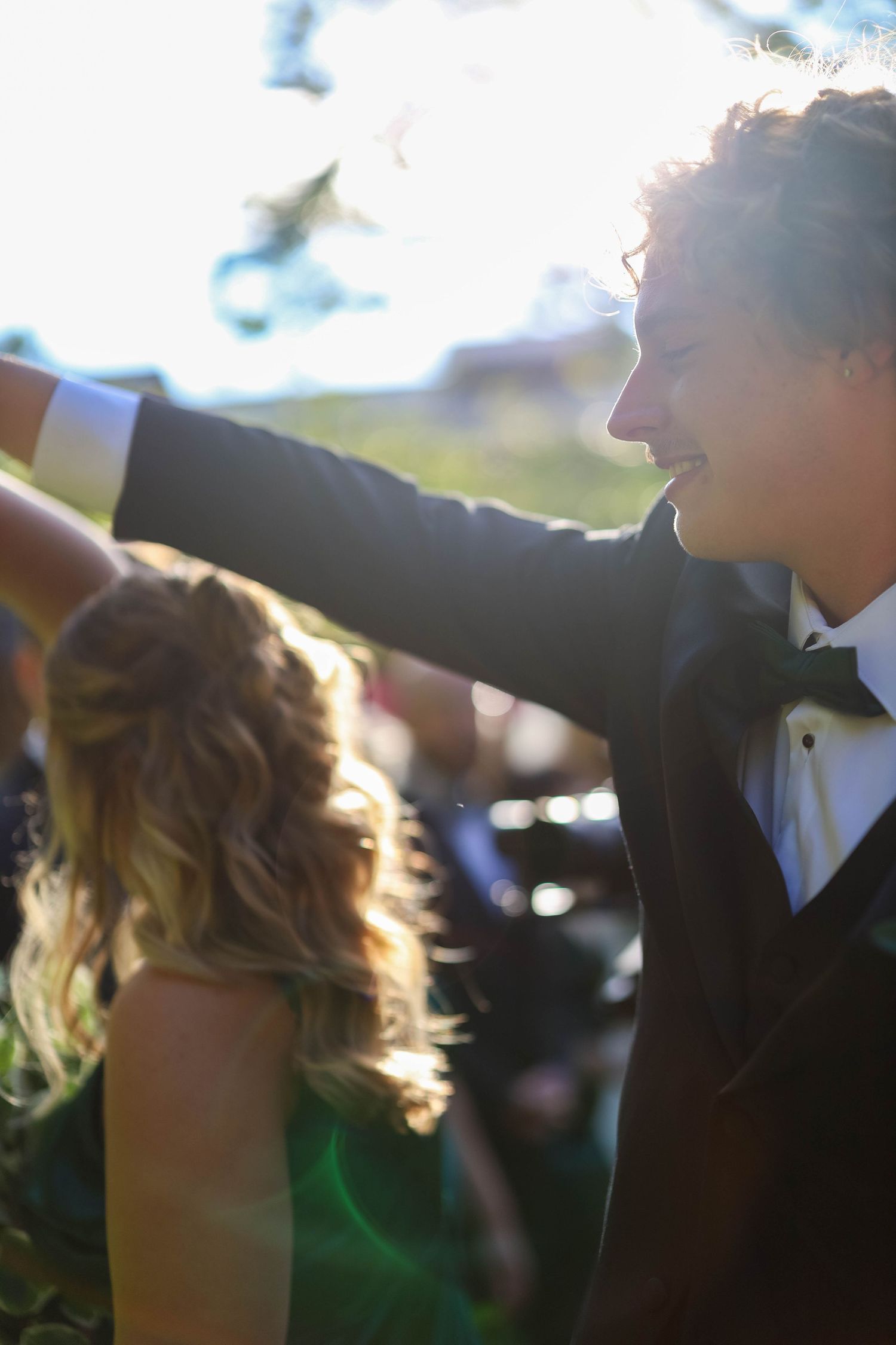 Sunlit silhouettes of a couple dancing together at an outdoor celebration with natural backlighting.