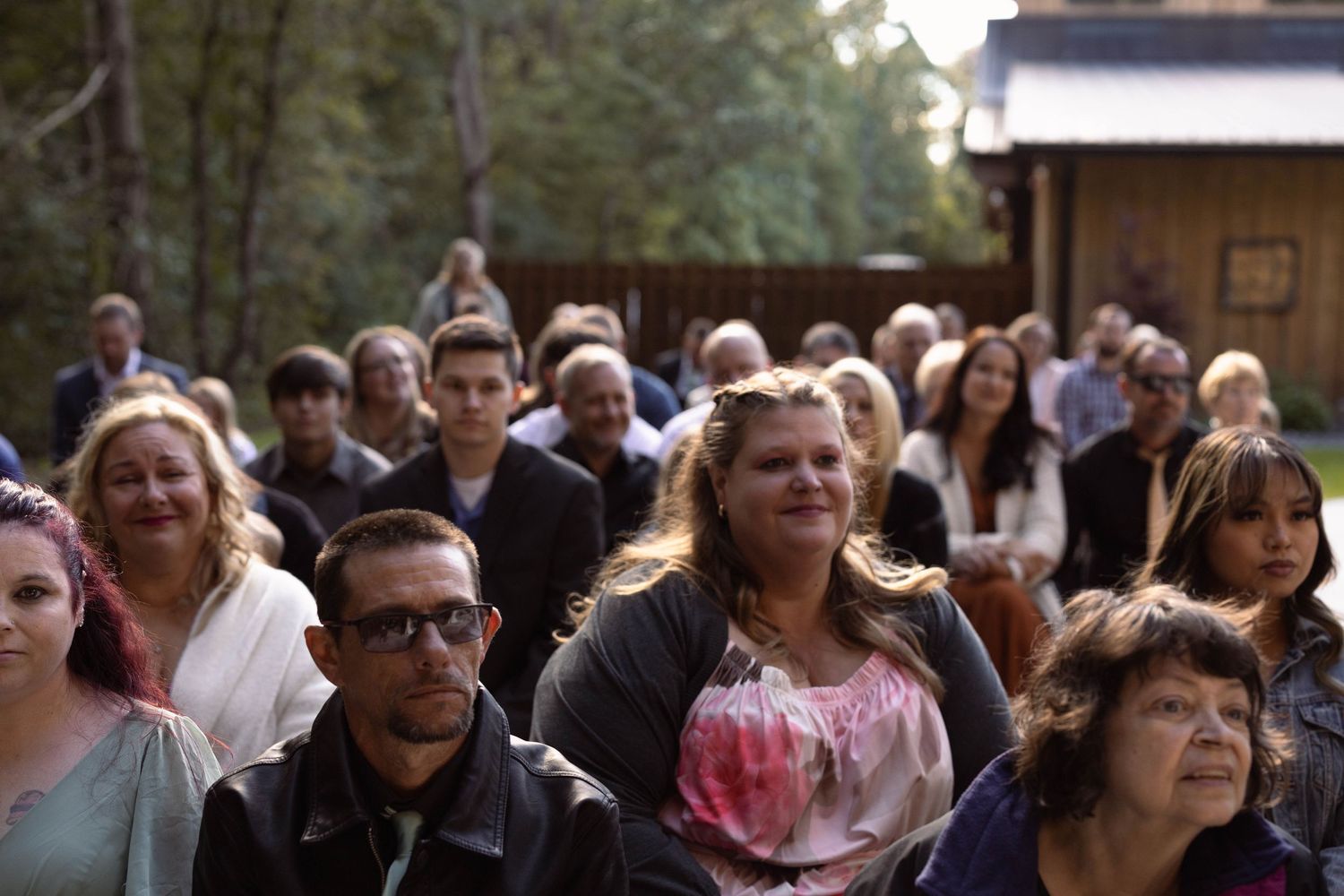 Outdoor wedding ceremony gathering with guests seated among trees and natural surroundings.