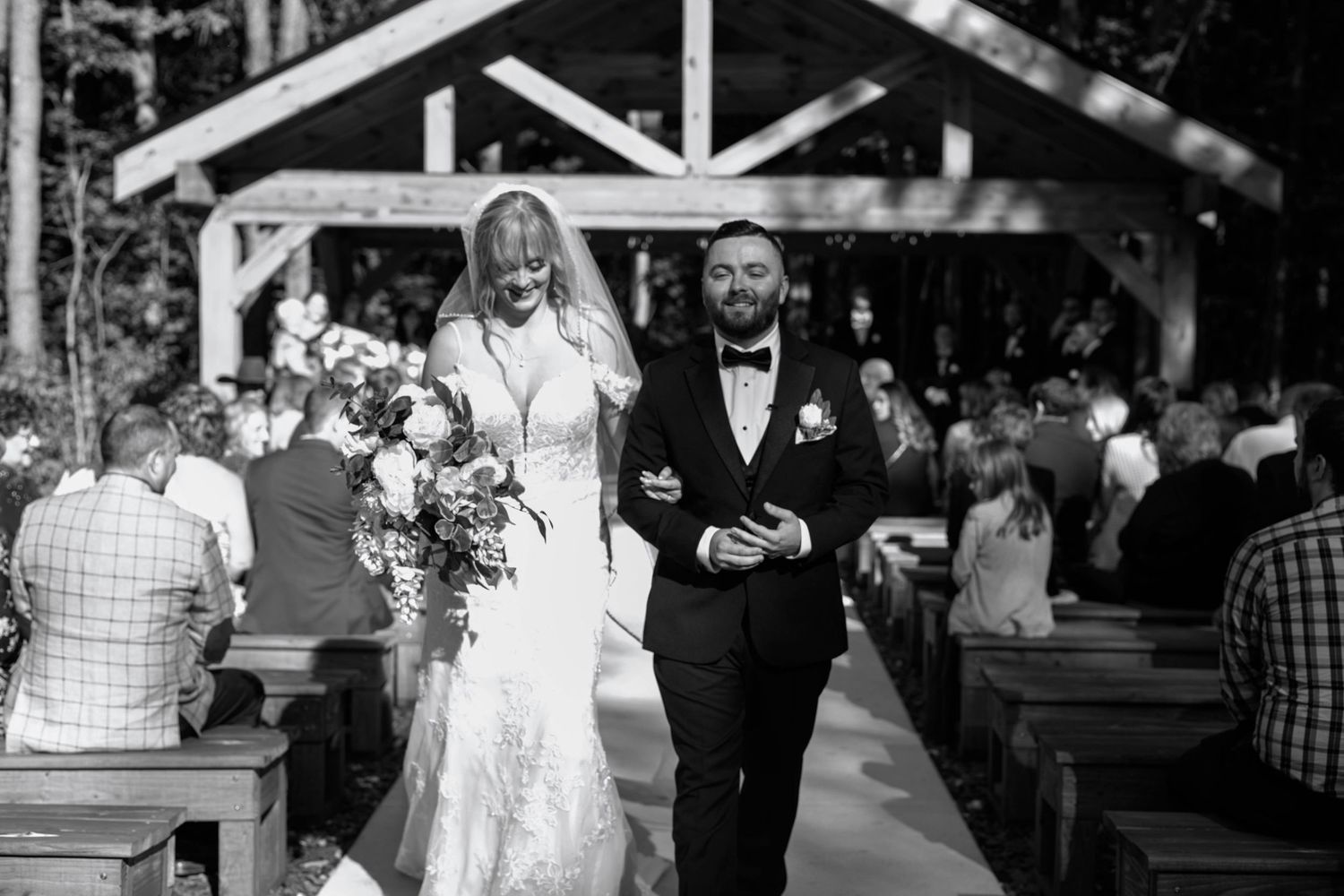 Wedding guests and ceremony under wooden pavilion in black and white photography.