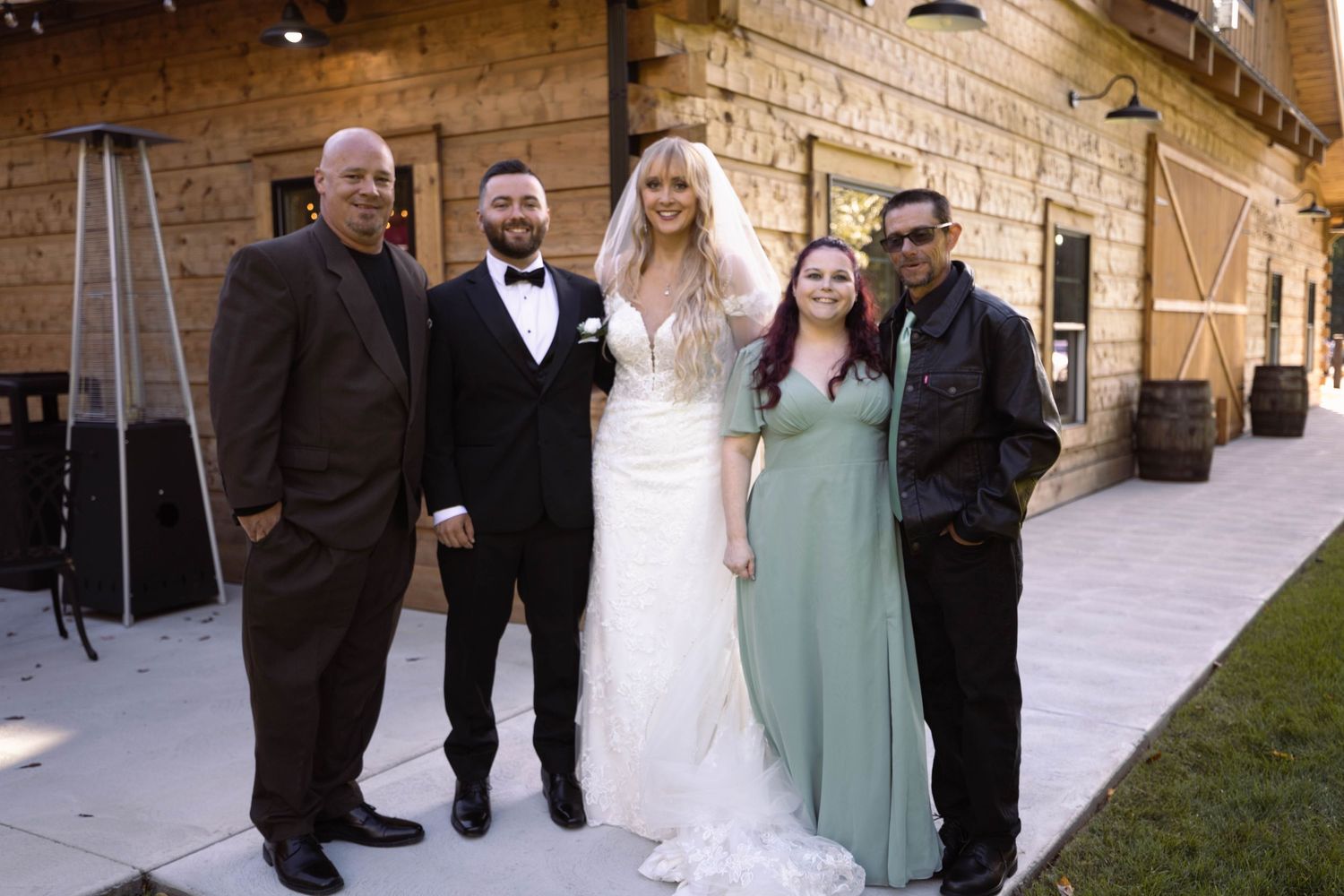 Wedding party poses together on stone patio outside elegant venue at sunset.