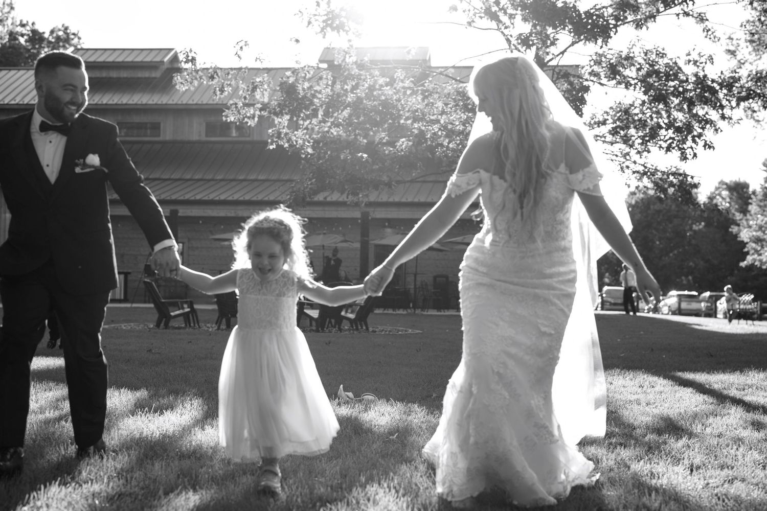 A black and white wedding photo shows a couple holding hands with a small child while walking outdoors.