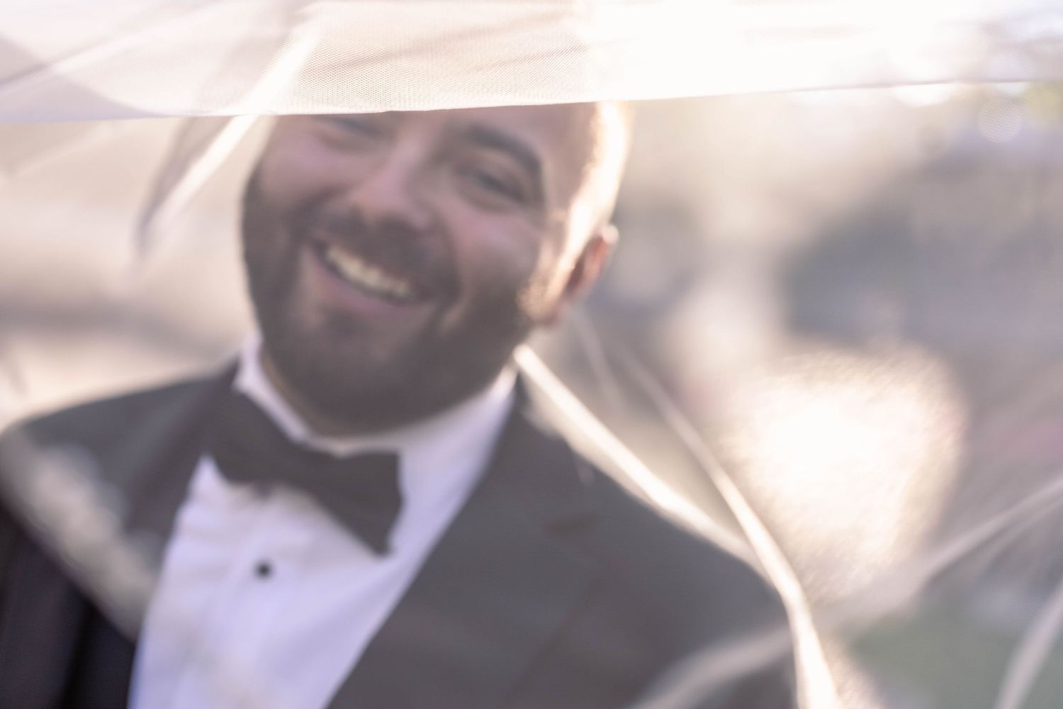 A soft focus portrait of someone wearing a black tuxedo and bowtie with a warm smile.