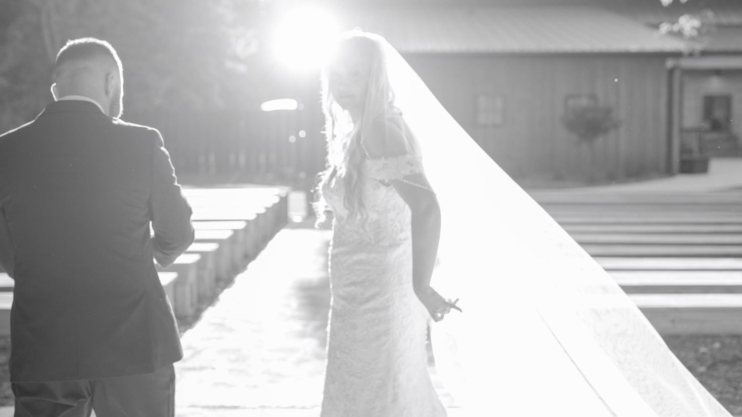 Silhouette of newlyweds with bride's veil flowing in golden sunlight at outdoor ceremony.