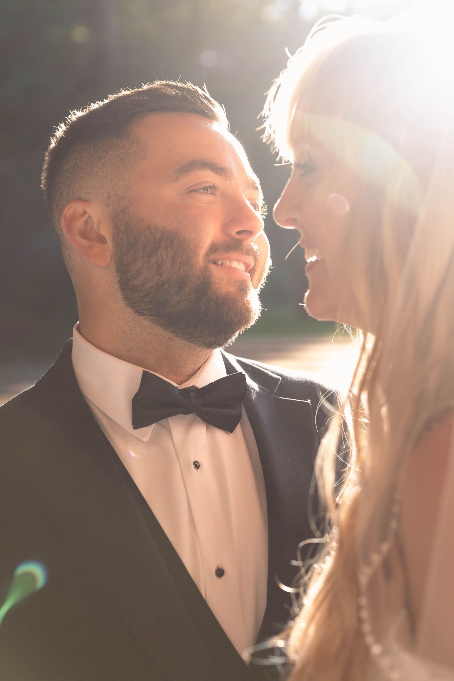 Intimate portrait of newlyweds sharing a joyful moment in warm sunlight with groom wearing a bowtie.