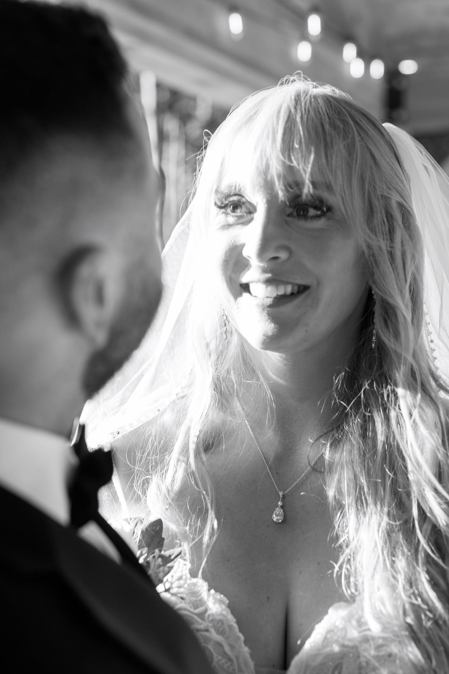 A candid black and white wedding portrait showing a radiant bride in a lace dress with flowing blonde hair.
