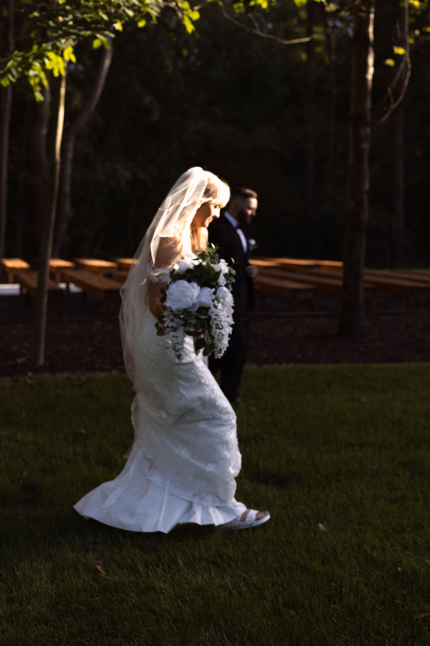 Bride in white dress sitting gracefully on grass in an outdoor garden setting.