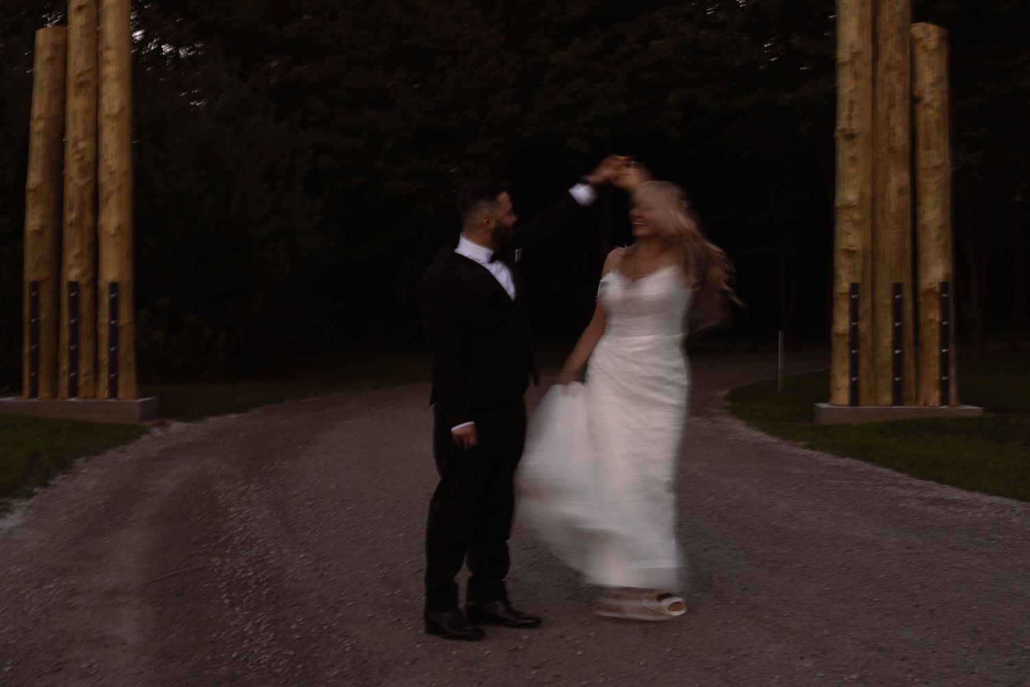 Wedding couple sharing intimate moment on tree-lined path at dusk.