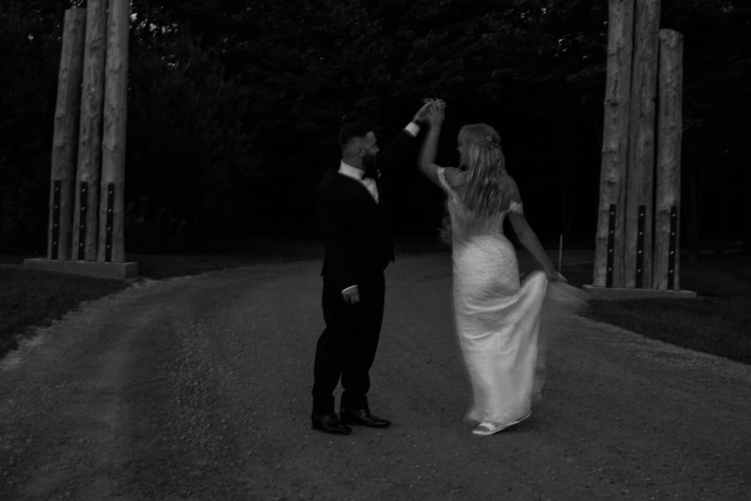 A couple dancing together under wooden pillars at night in black and white.