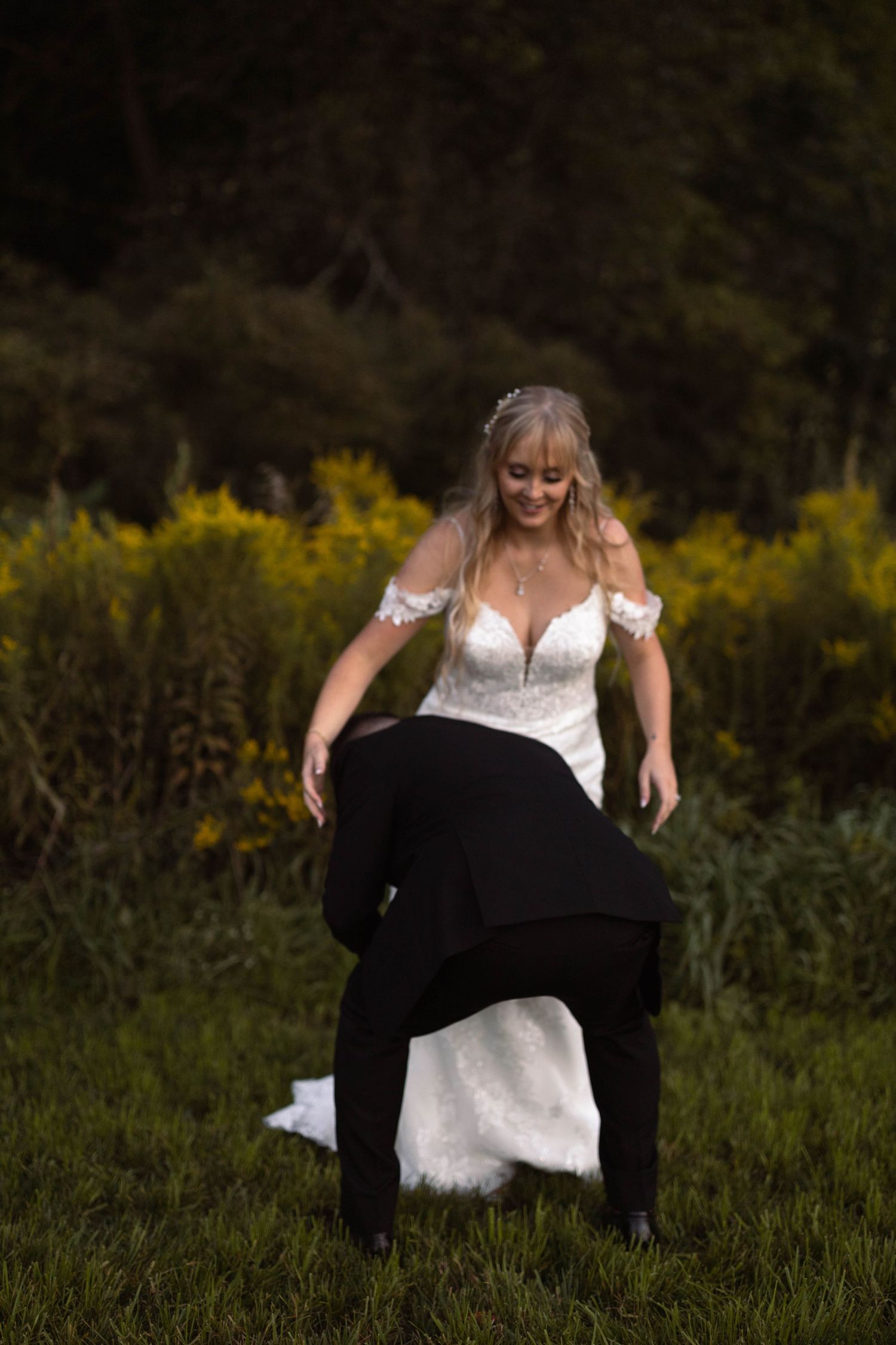 Bride in lace wedding dress playfully posing in field with yellow wildflowers.