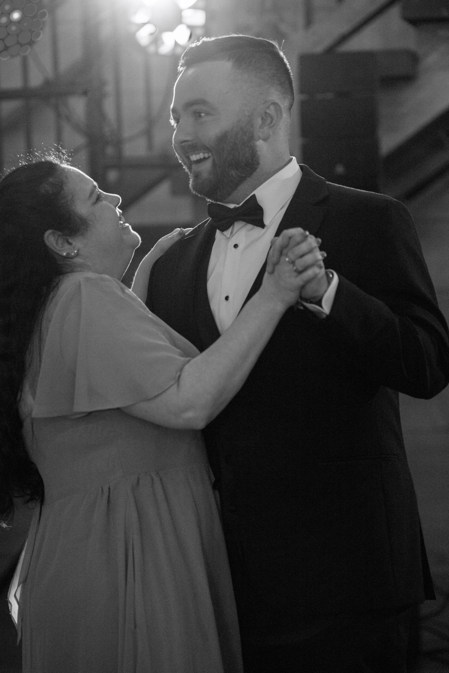 A couple shares an intimate dance moment at a formal event in black and white photography.
