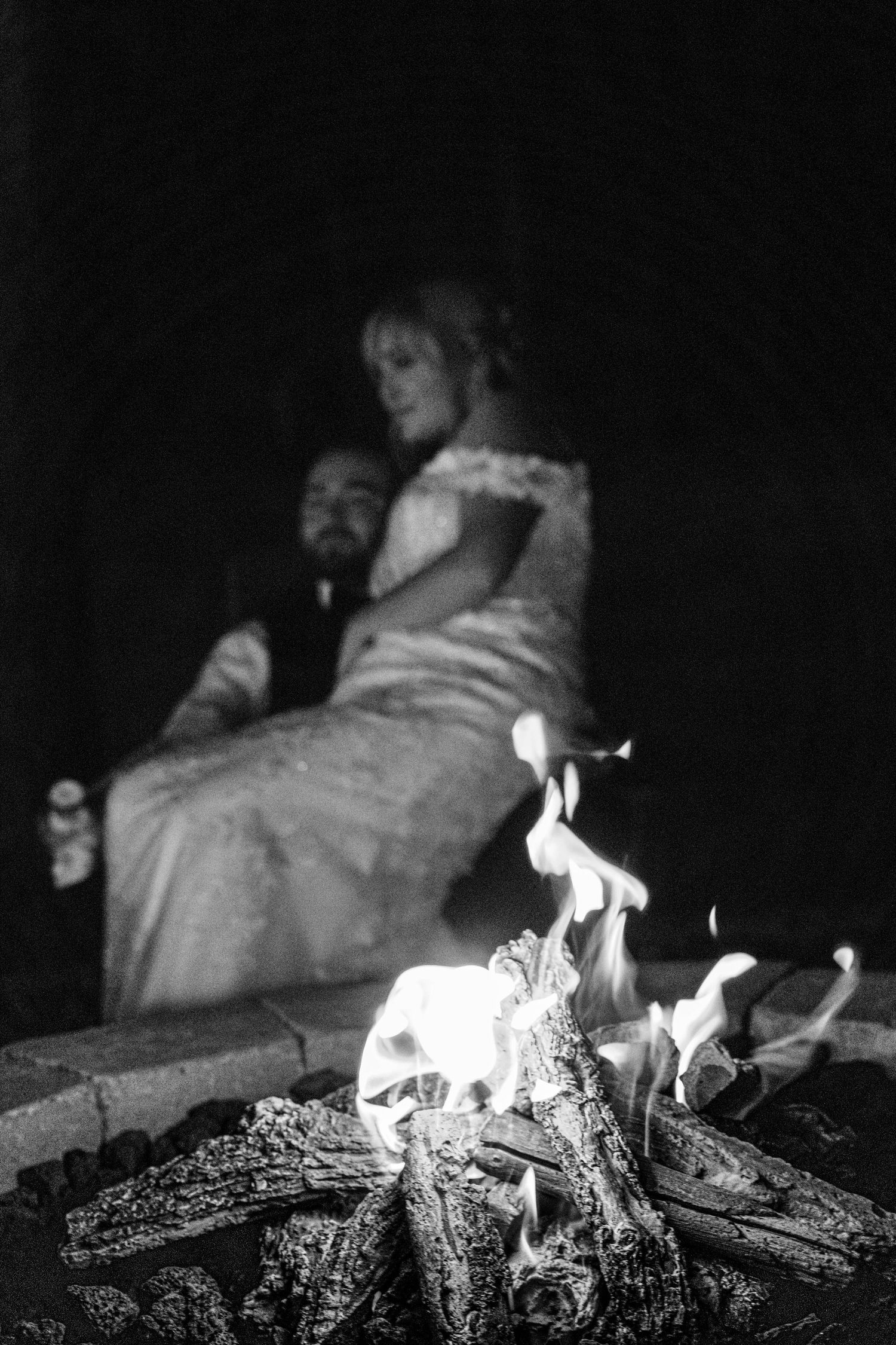 A romantic silhouette of a couple sitting by a glowing campfire at night.